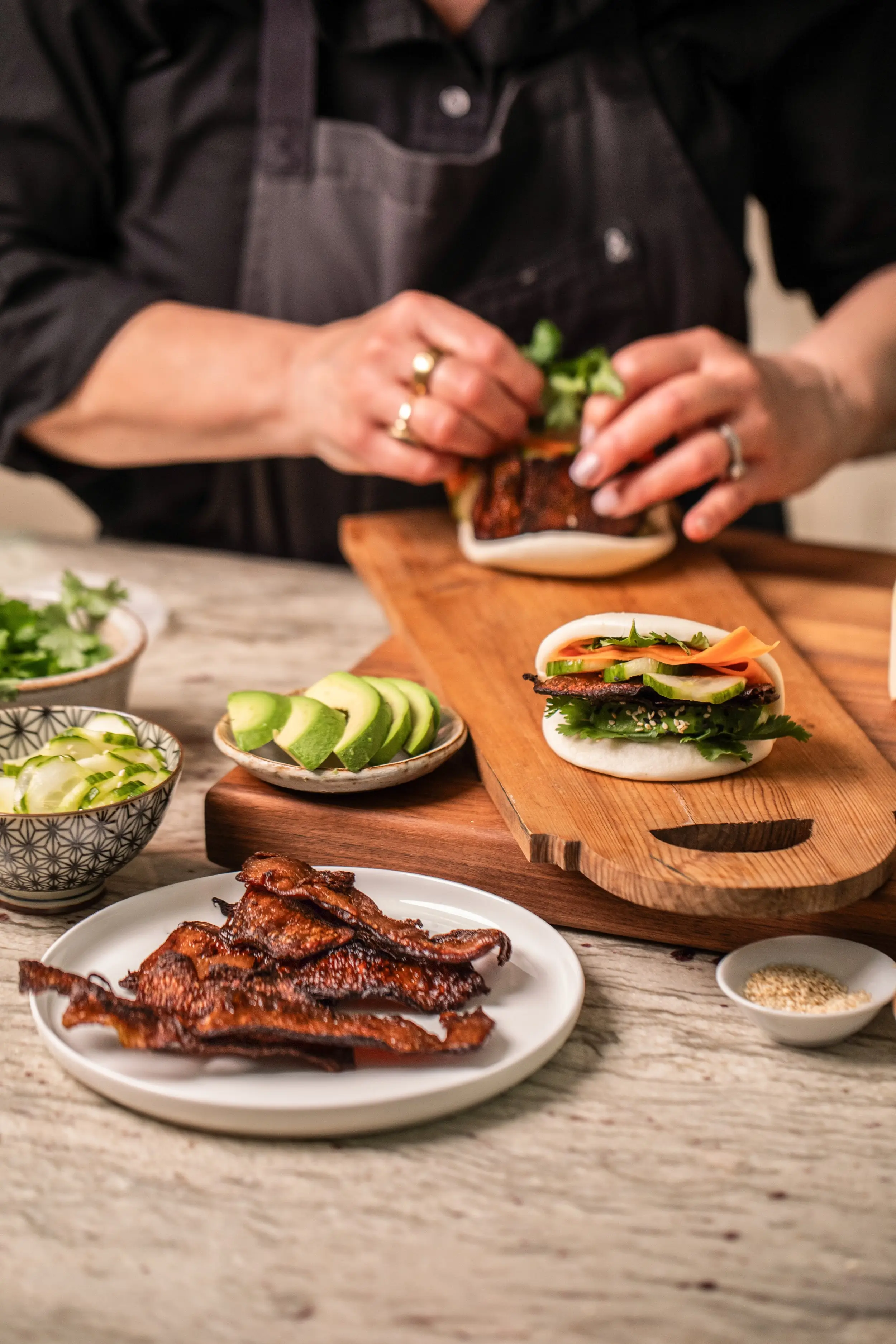 A close-up of cooked myBacon slices in the foreground while a Bao Bun is being built in the background