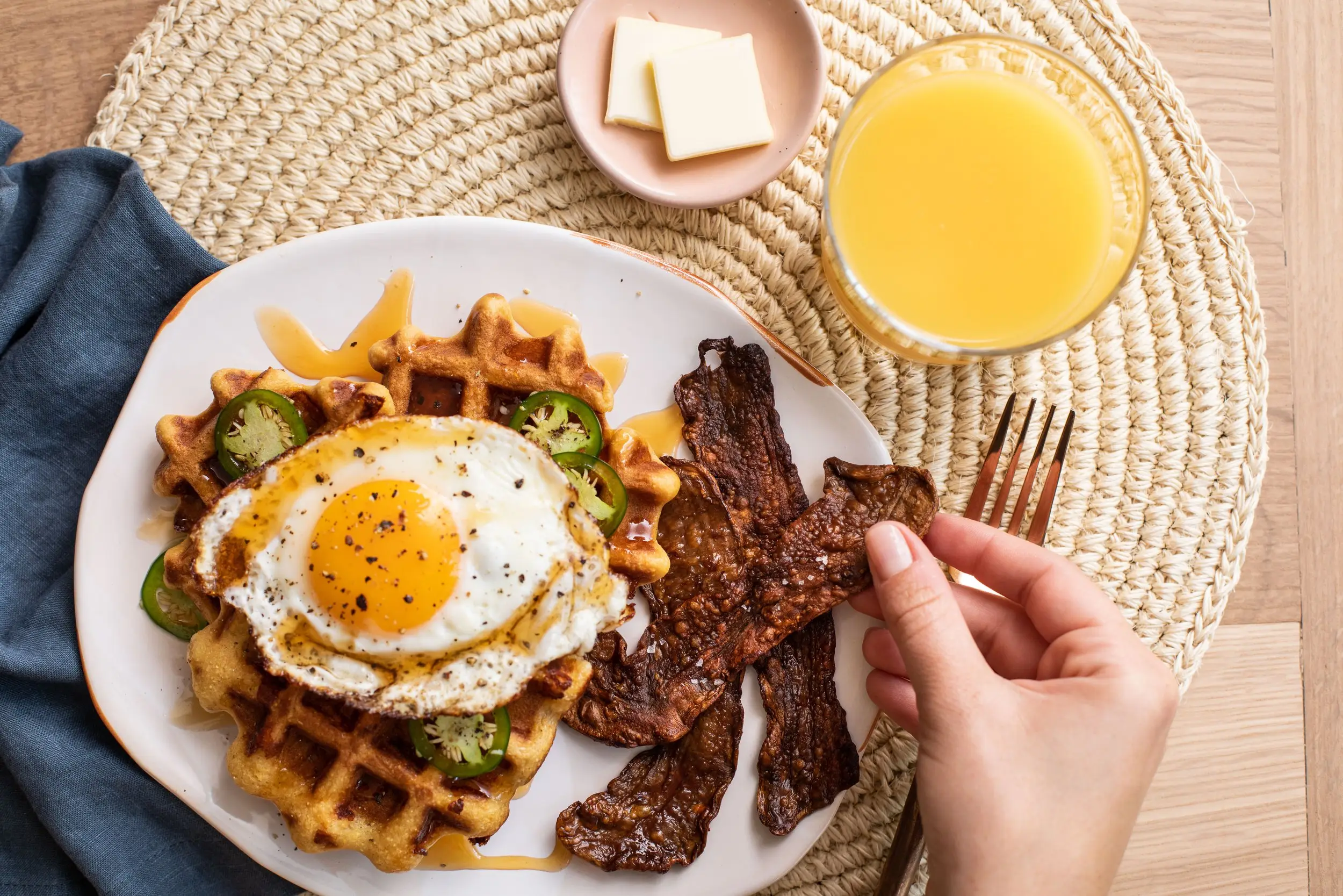 Hand grabbing MyBacon from plate filled with waffles and an over-easy egg