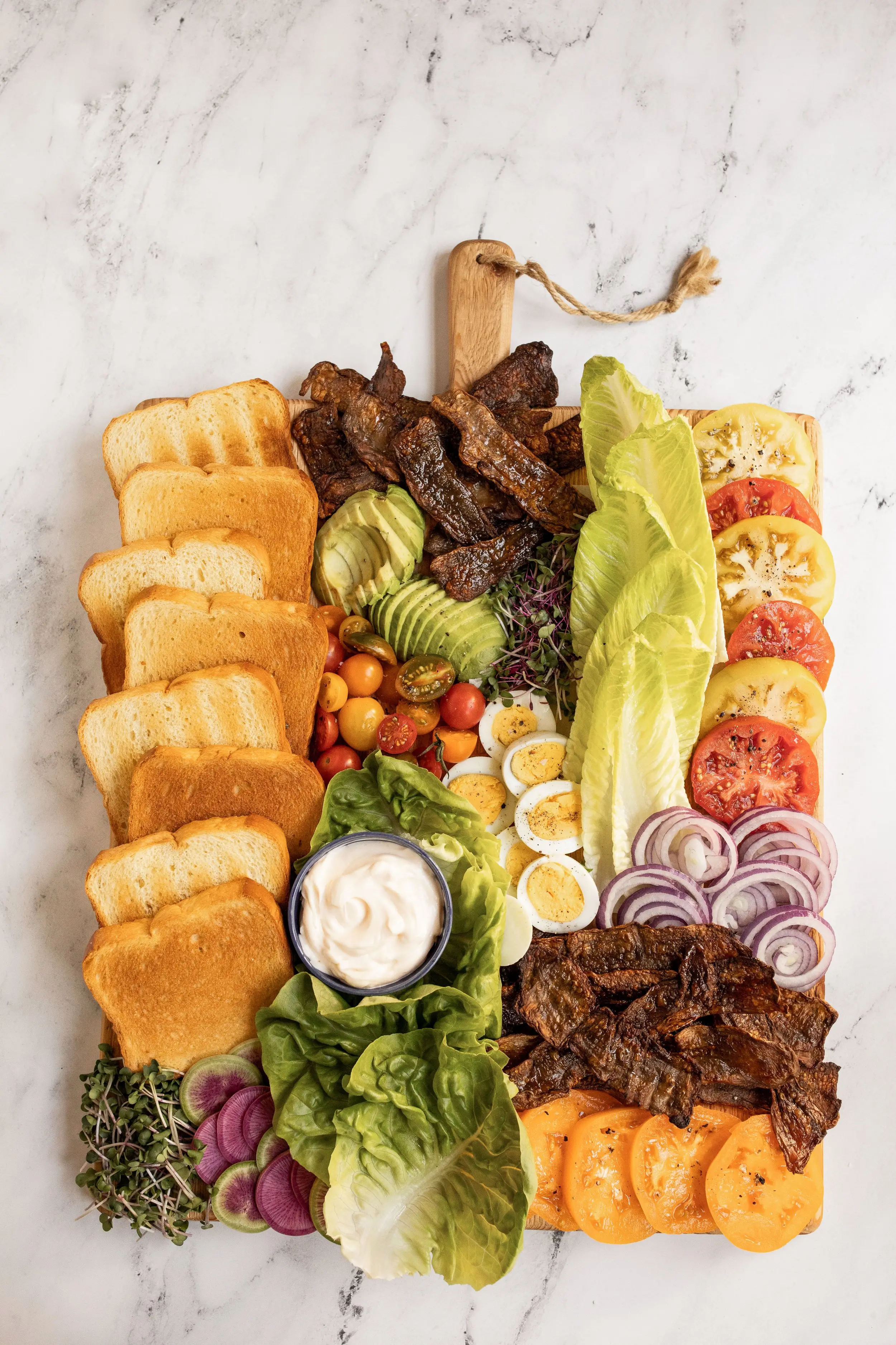 A board spread with bread, MyBacon, Avocado, Egg, Lettuce, tomato and other BLT fixings